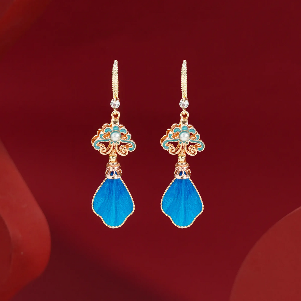 Front view of blue silk velvet drop earrings on a red background
