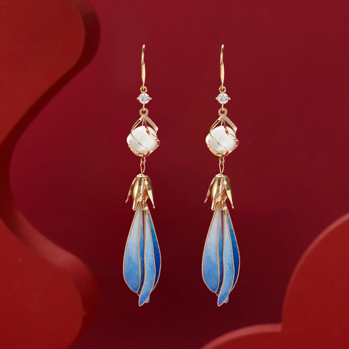 Front view of blue magnolia silk velvet drop earrings on a red background