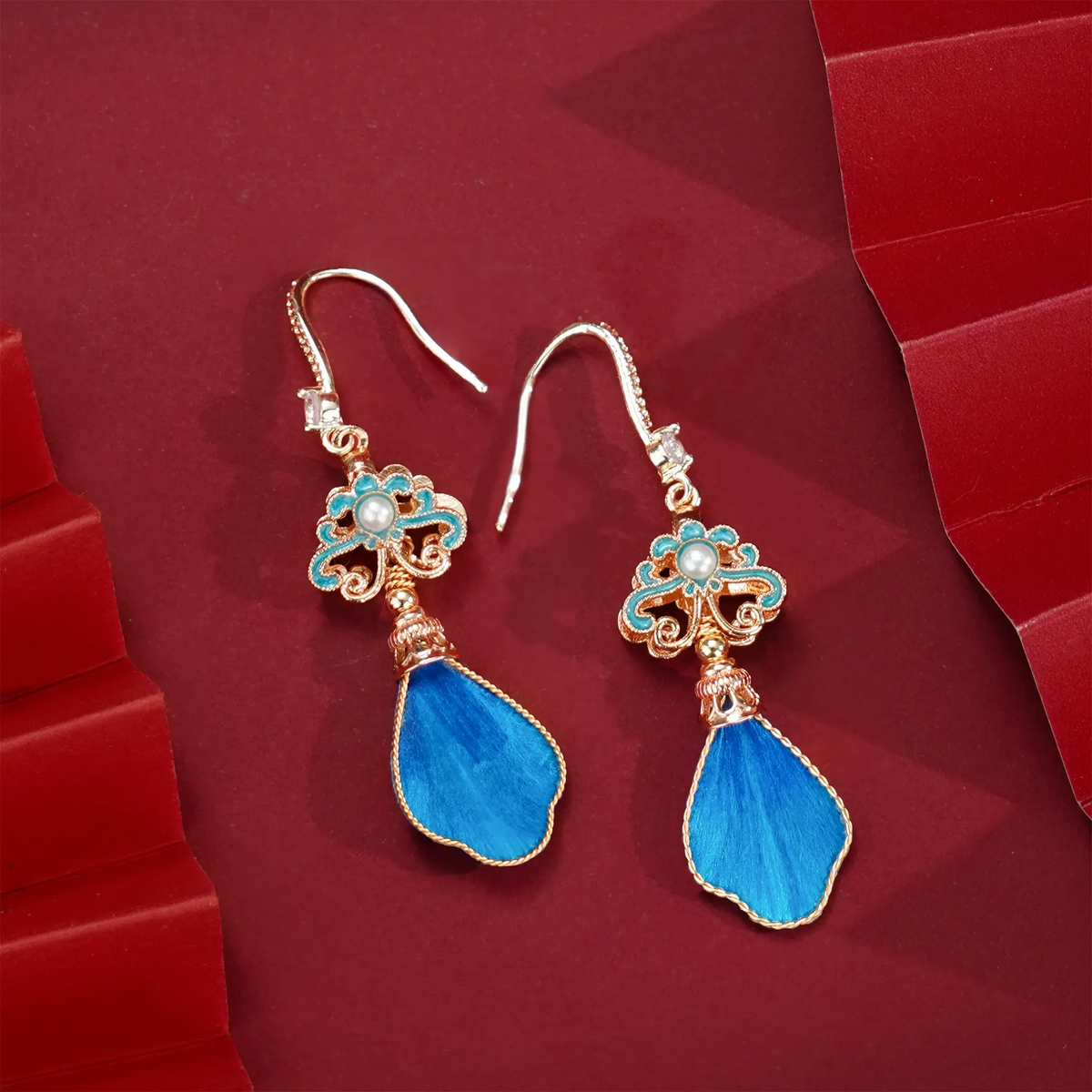 Angled view of blue silk velvet drop earrings showing gold-tone edging