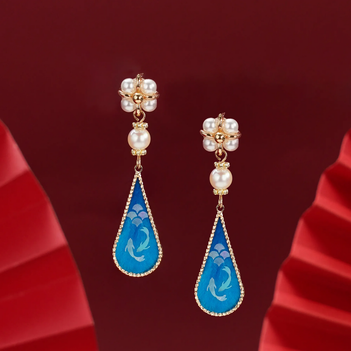 Angled view of twin fish silk velvet drop earrings on red