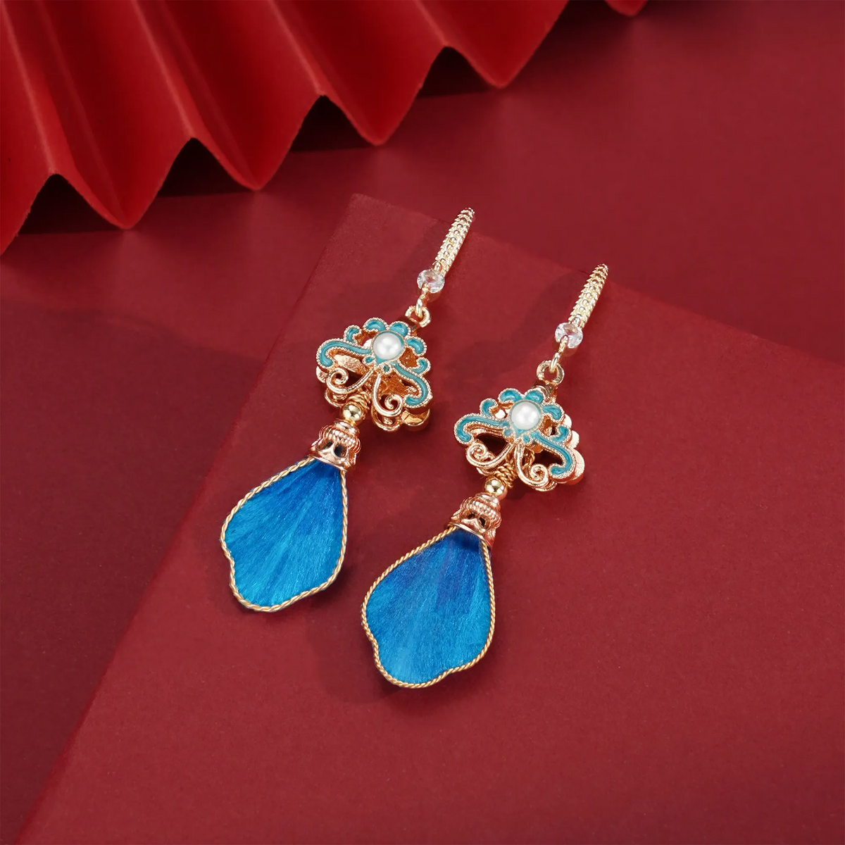 Blue silk velvet drop earrings on a sculptural red display