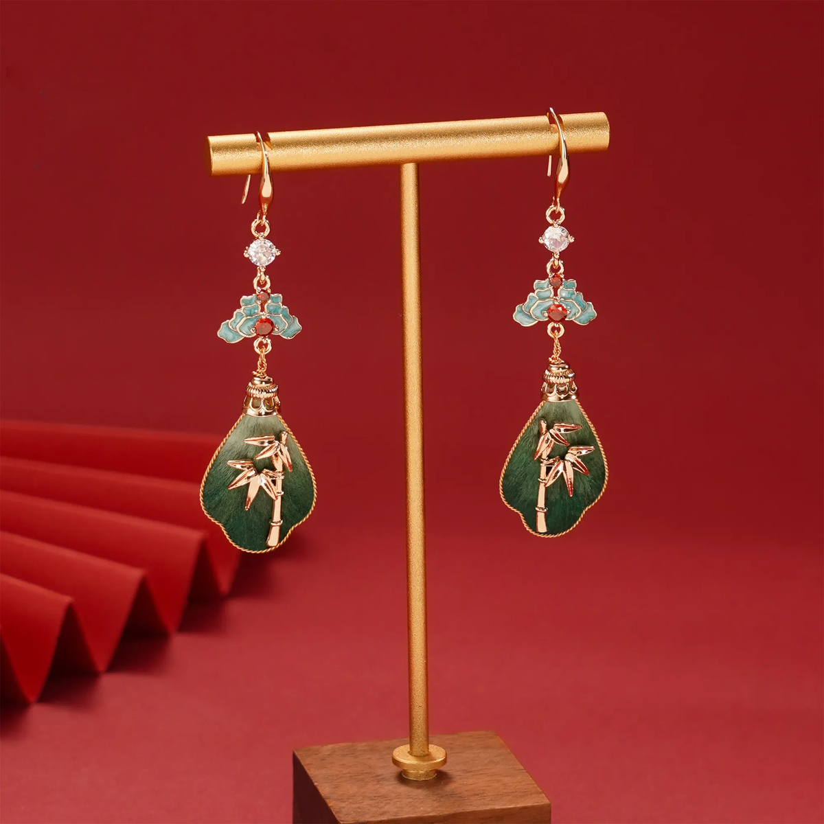 Pair of green bamboo silk velvet earrings hanging on a stand against red