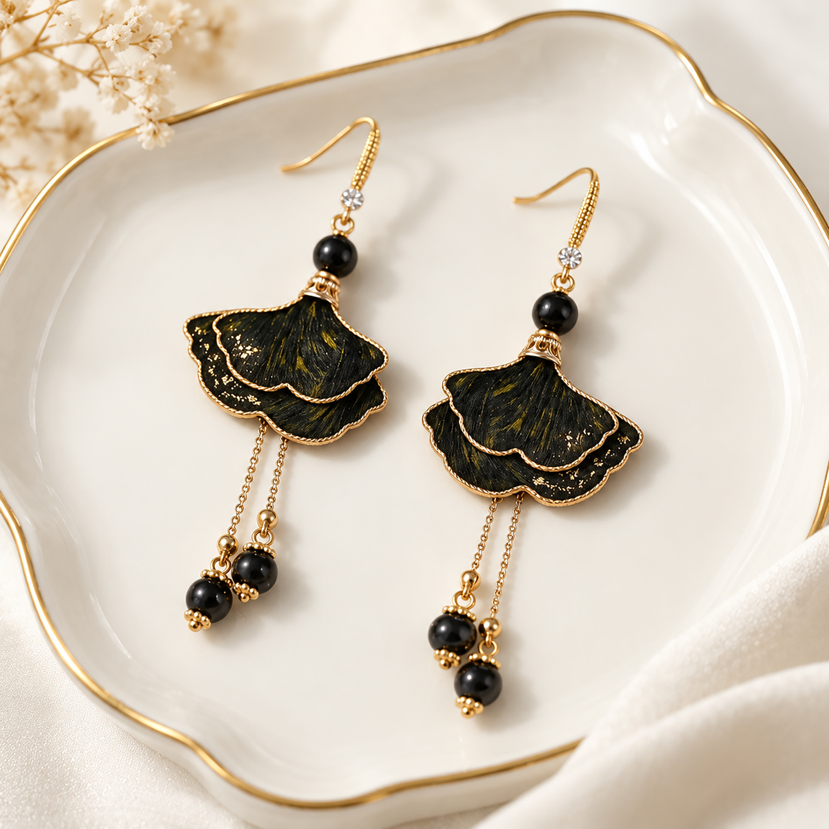 Ink-dyed ginkgo silk drop earrings with gold flecks and black beads on a cream dish