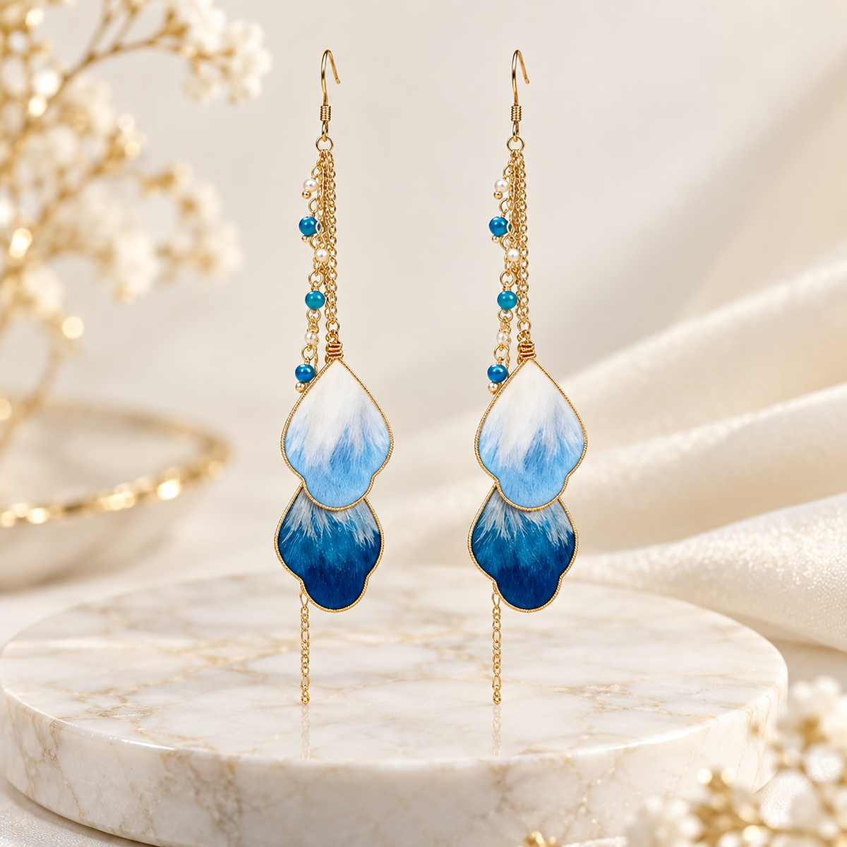 Second view of the blue vine silk drop earrings on a cream marble plinth, fishhook wires visible