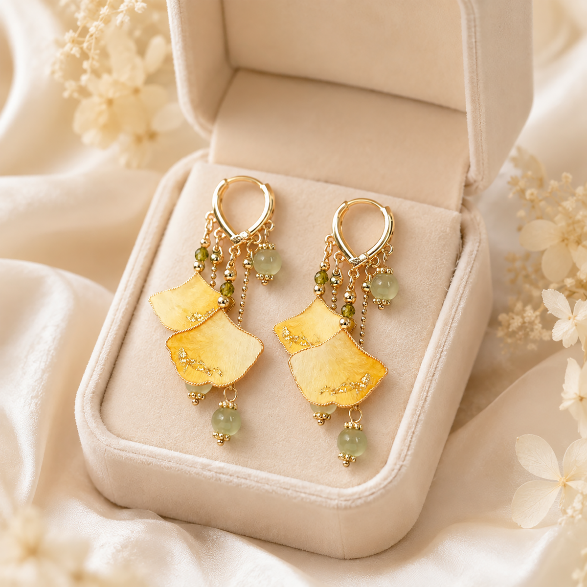 Pair of golden ginkgo silk velvet dangle earrings displayed in a cream jewellery box