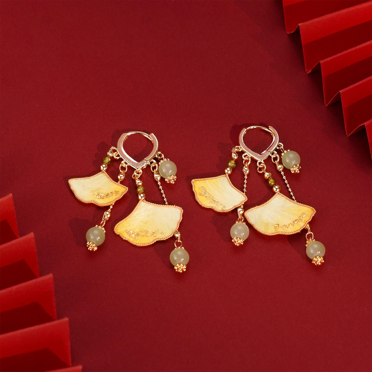 Pair of golden ginkgo silk velvet dangle earrings arranged on a red background
