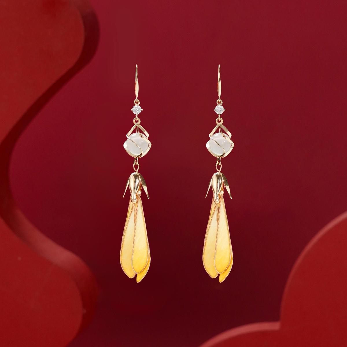 Front view of Golden Magnolia silk velvet drop earrings against a deep red background