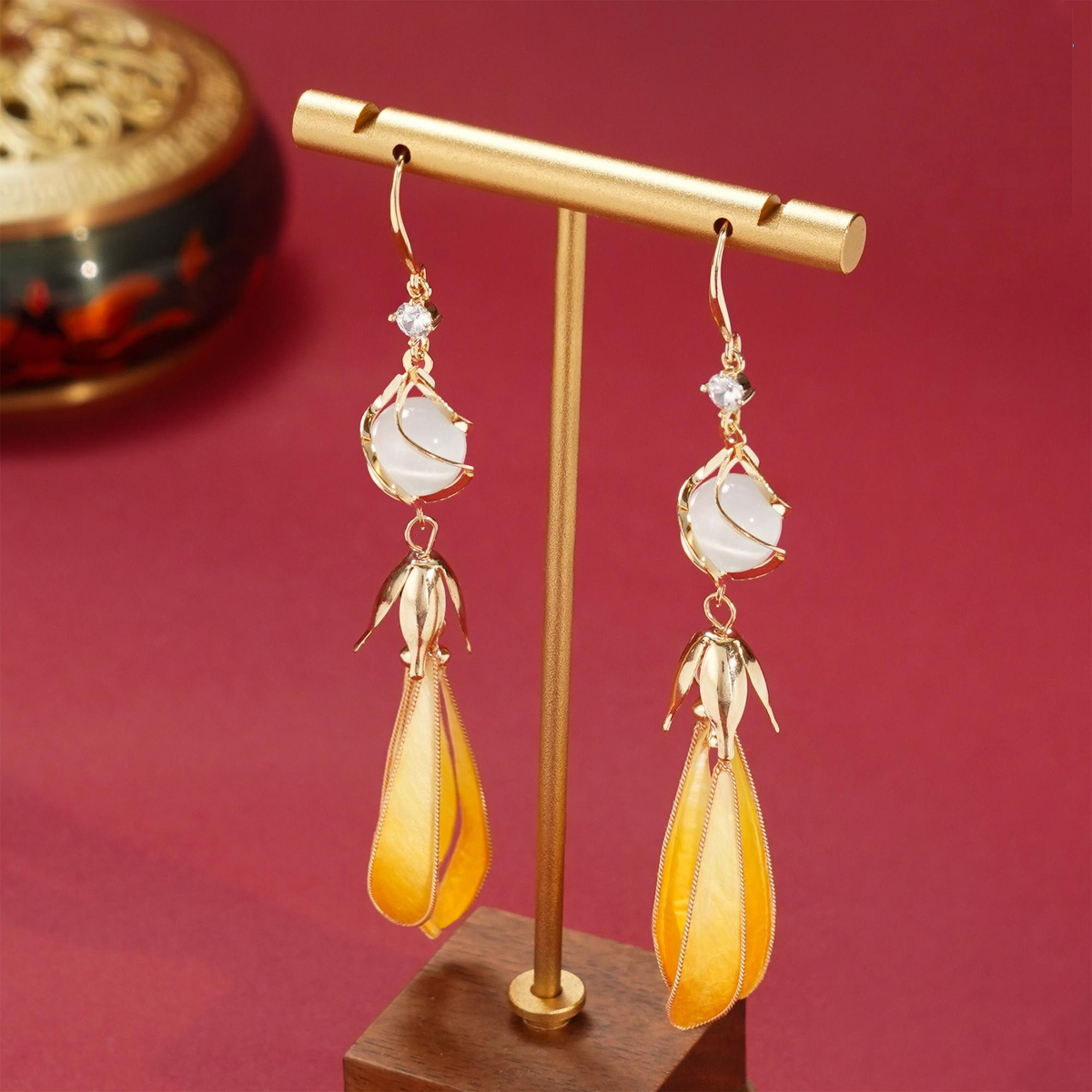 Pair of long golden magnolia silk velvet earrings displayed on a gold stand