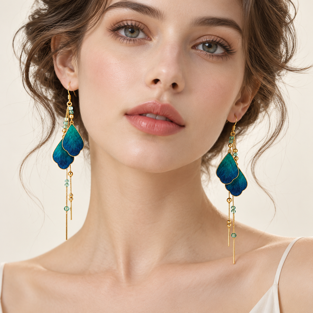 Model wearing blue and teal mulberry silk Ronghua earrings with layered teardrop shapes, gold-tone edging, dangling chains and green beads.