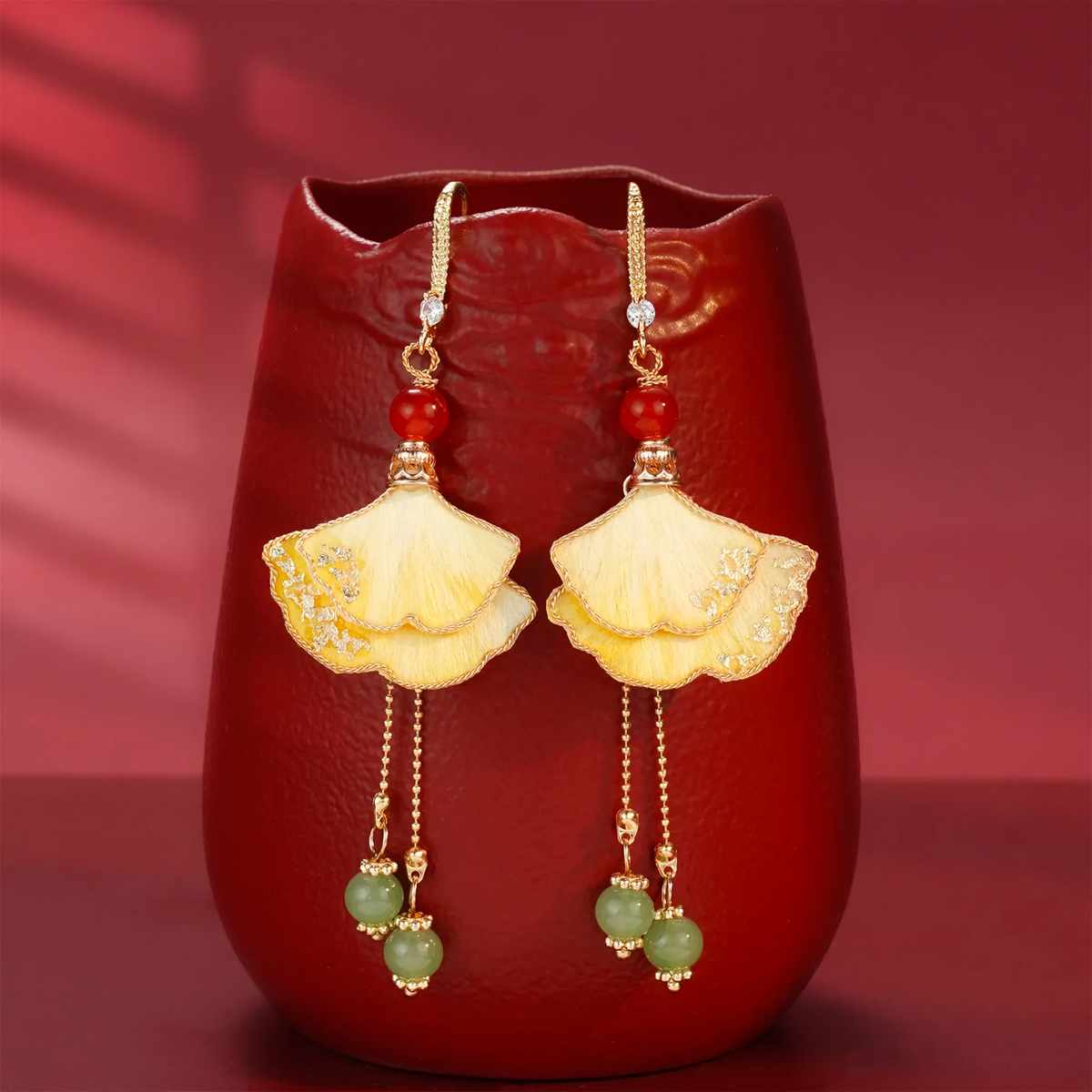 Golden Yellow Ginkgo Ronghua earrings displayed on a red ceramic stand