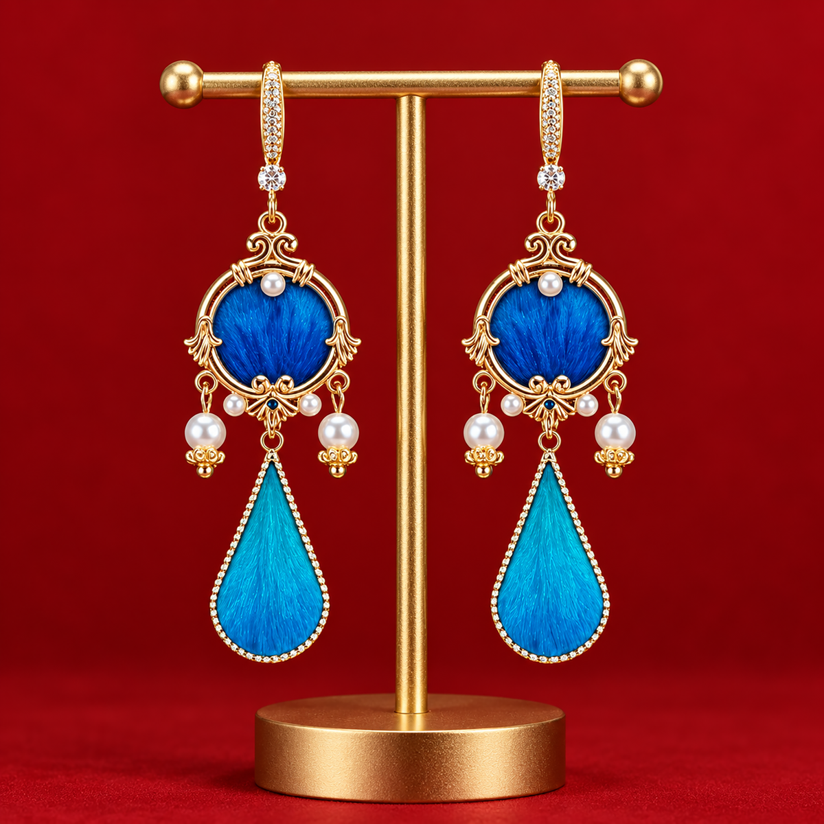 Blue circular silk motifs and turquoise teardrops in gold-tone frames on a stand against red fabric