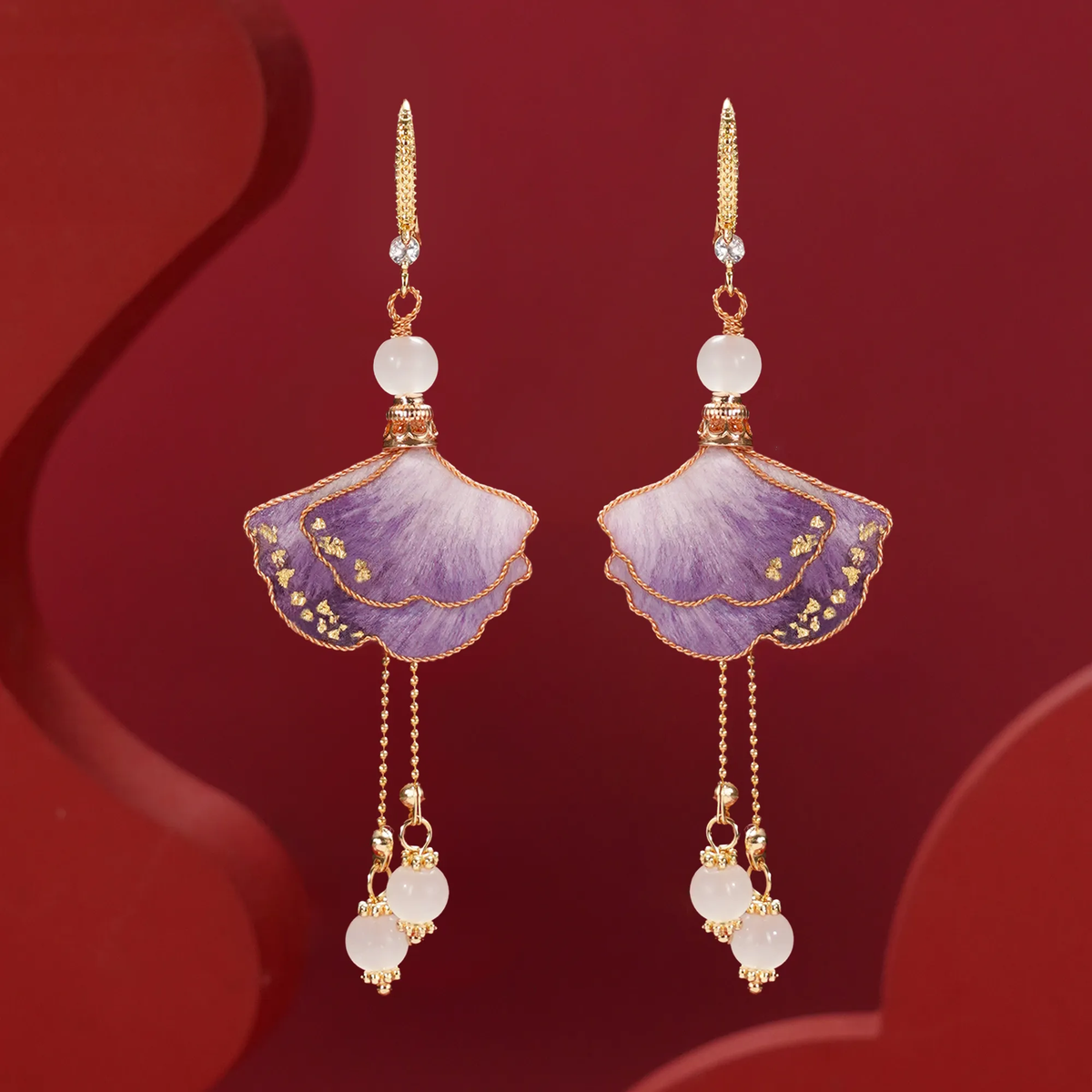 Pair of purple ginkgo Ronghua drop earrings on a deep red background