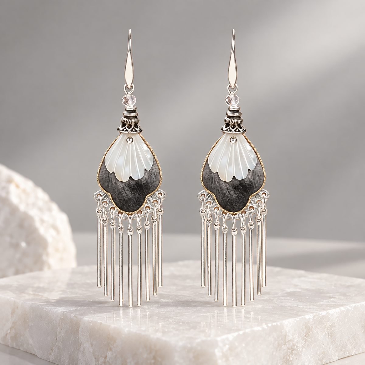 Black and ivory silk teardrops with silver-tone fringe displayed upright on pale stone