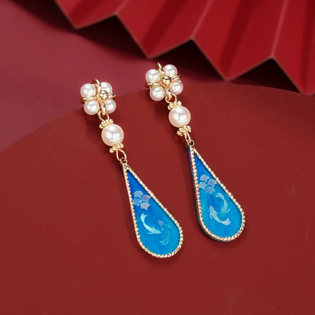Front view of blue twin fish silk velvet drop earrings on red