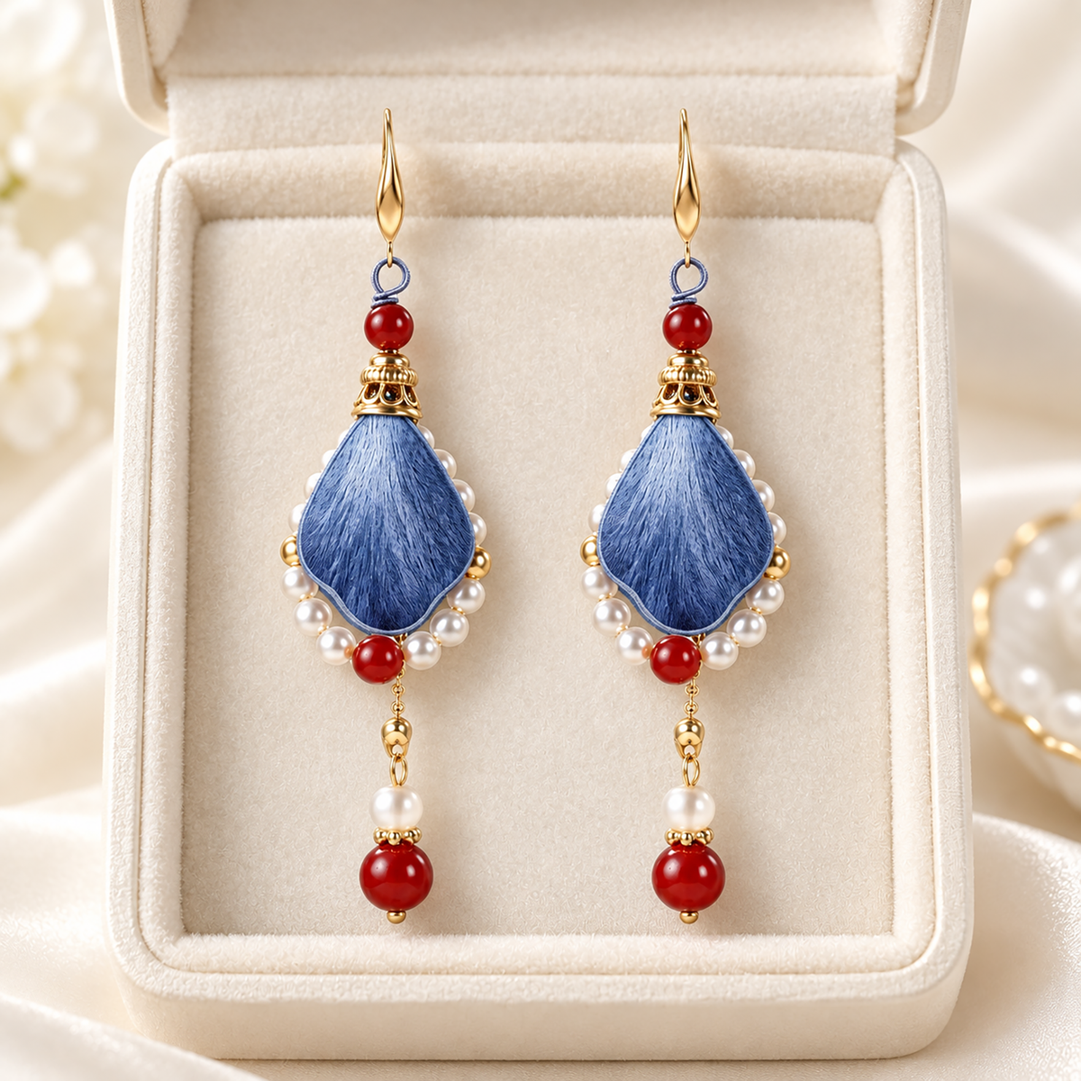 Pair of blue-red mulberry-silk drop earrings with pearl-like frames and fishhook wires, in a cream jewelry box