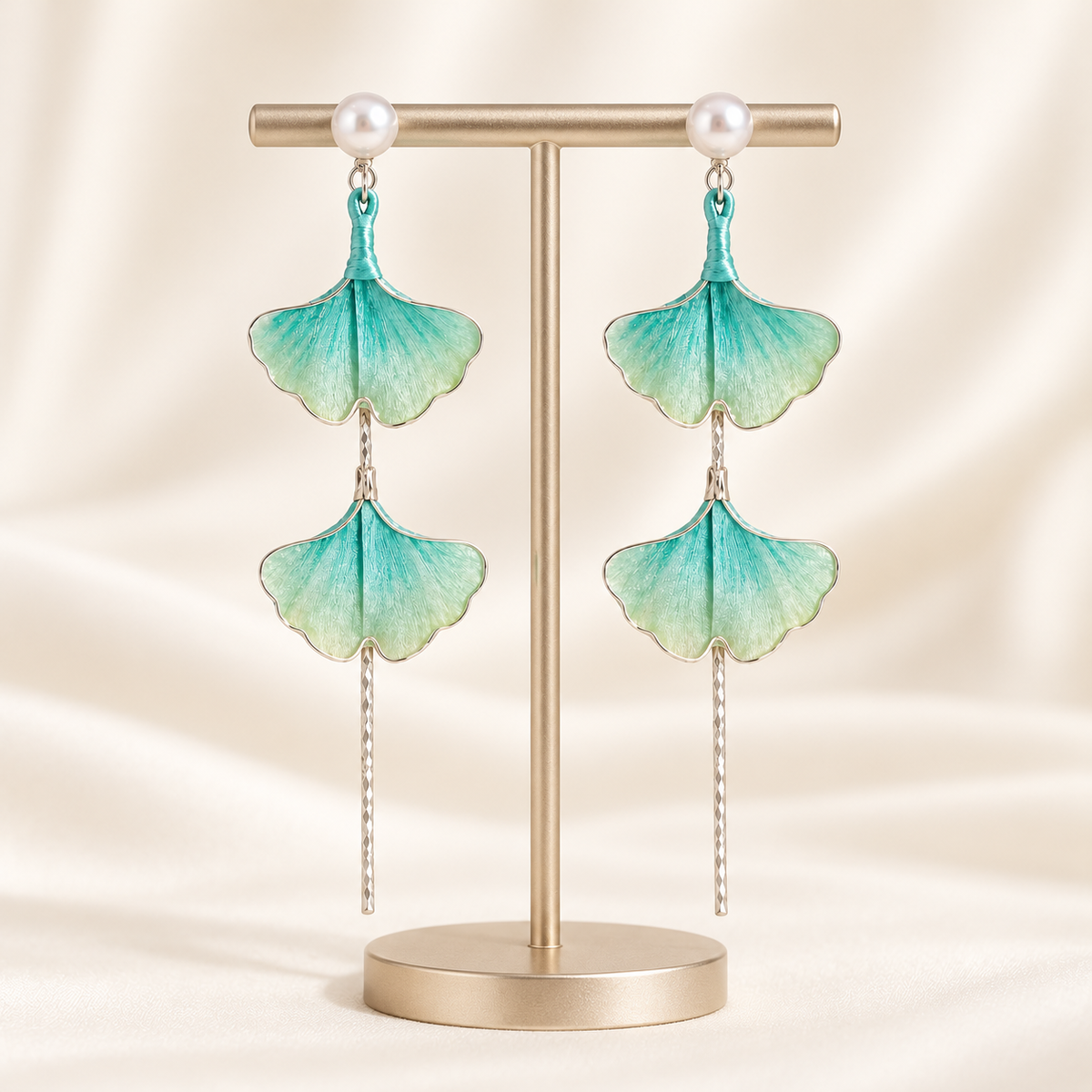 Teal green ginkgo Ronghua stud earrings on a display stand