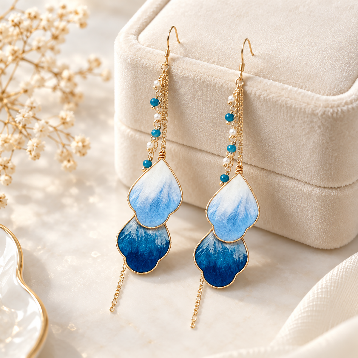 Blue vine silk Ronghua drop earrings standing beside a cream jewelry box, fishhook wires visible