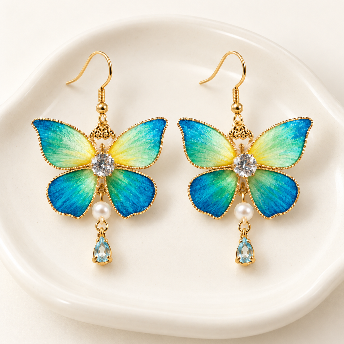 Blue-green butterfly Ronghua drop earrings on a ceramic dish