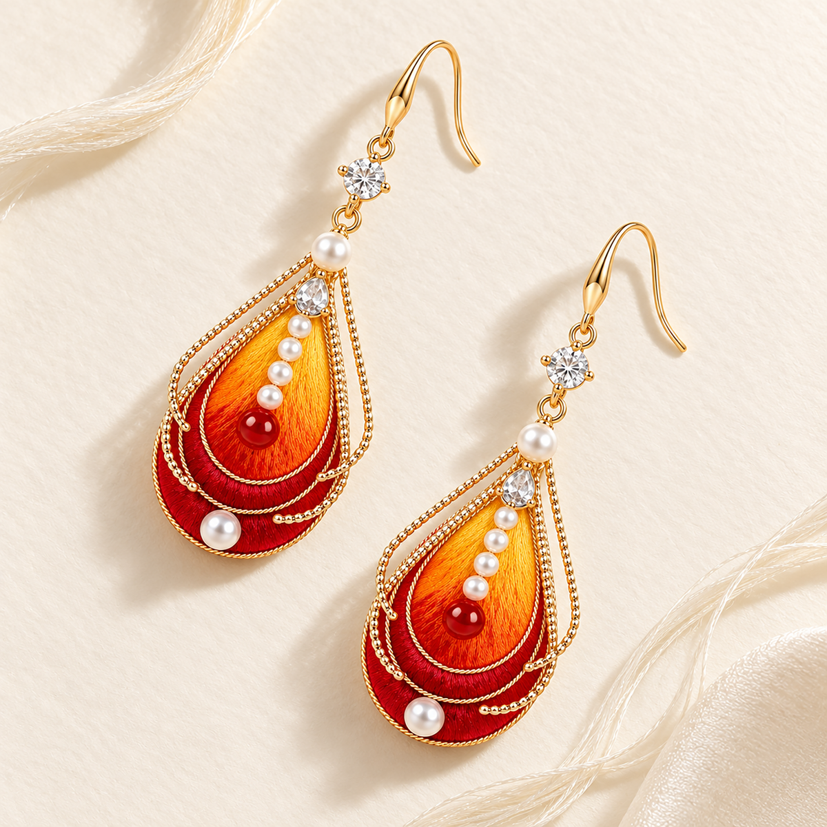 Pair of vermilion-bird silk Ronghua drop earrings with fishhook wires on a cream background