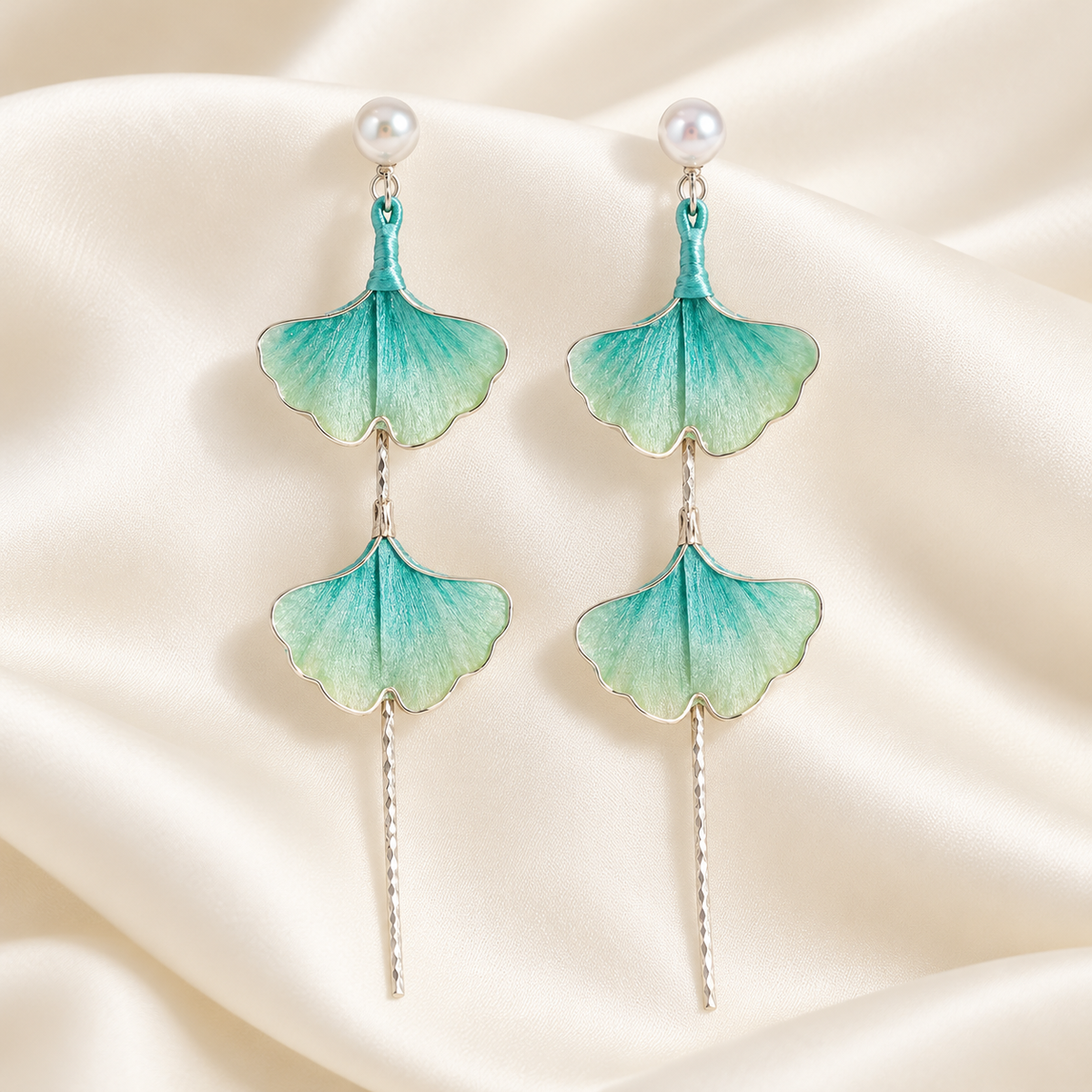 Teal green ginkgo silk Ronghua stud earrings close-up on satin