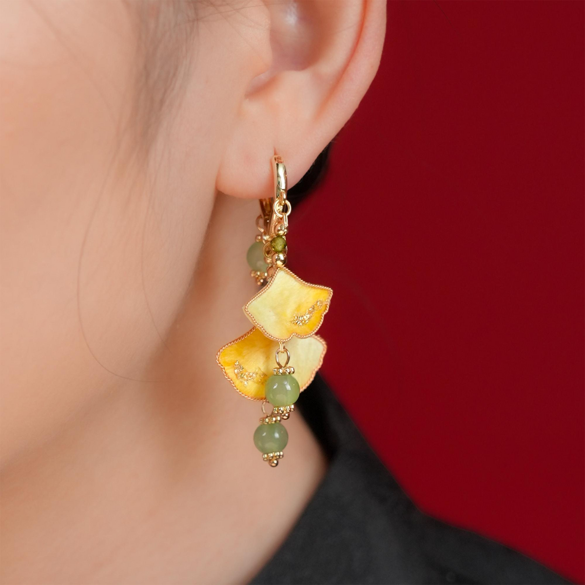 Golden ginkgo silk velvet dangle earring worn on the ear against a red background