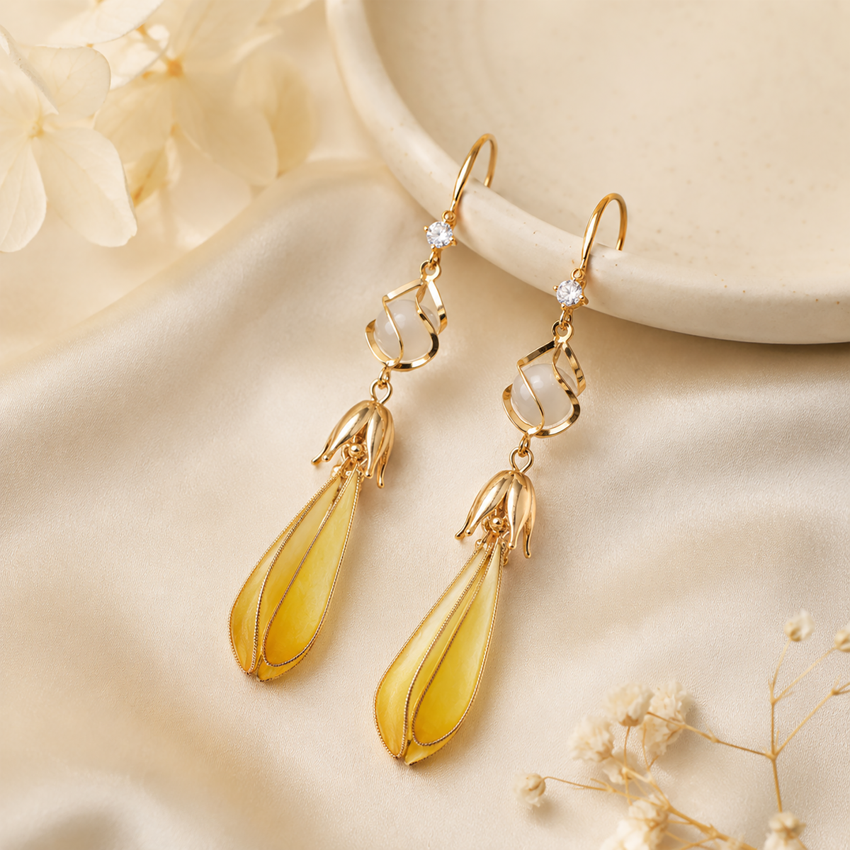 Pair of golden yellow magnolia silk velvet drop earrings displayed on ivory satin