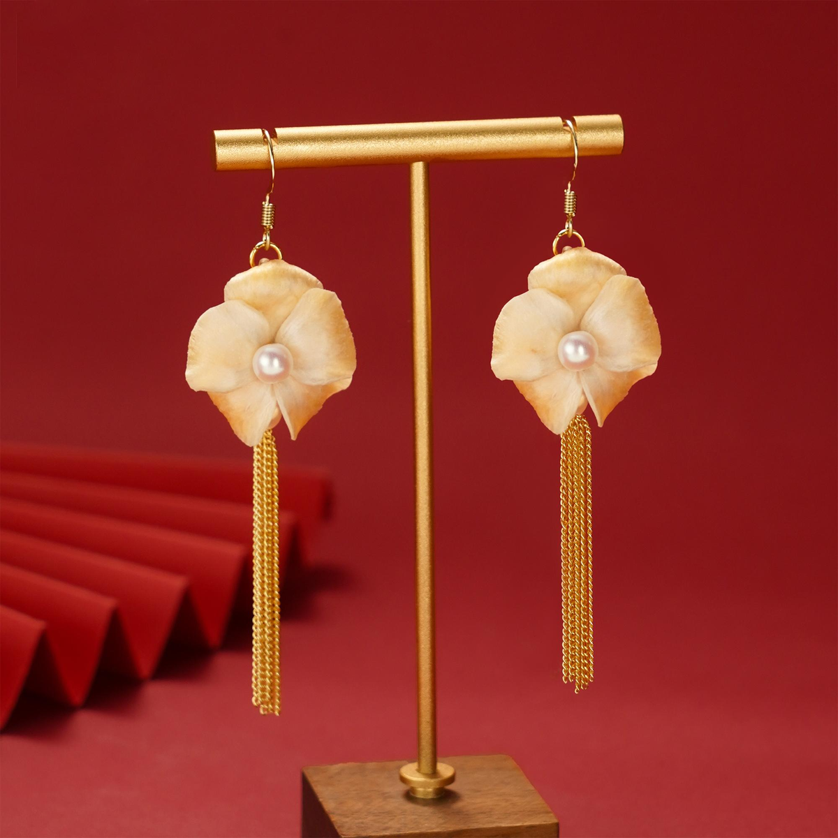 Ivory magnolia flower tassel earrings with gold-tone chains on a cream stone plinth