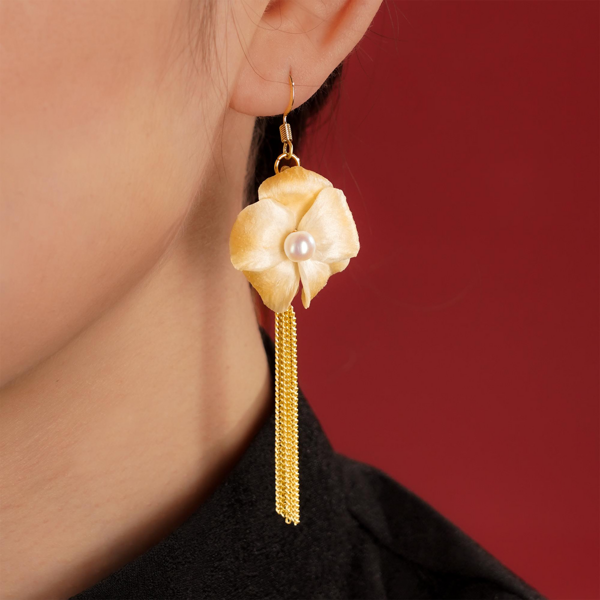 Pair of ivory magnolia silk velvet tassel earrings on a gold stand against a red background