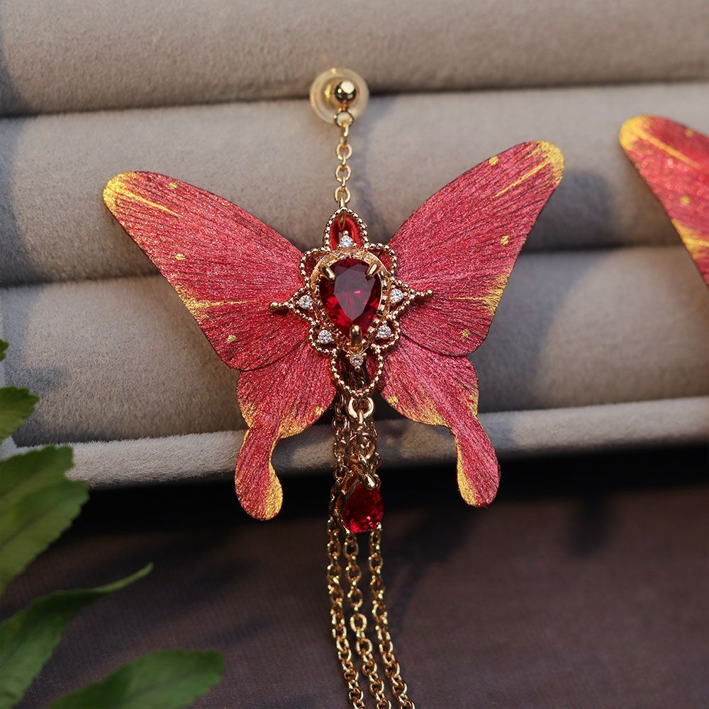 Close-up of a red silk butterfly earring with teardrop crystal and gold-toned setting