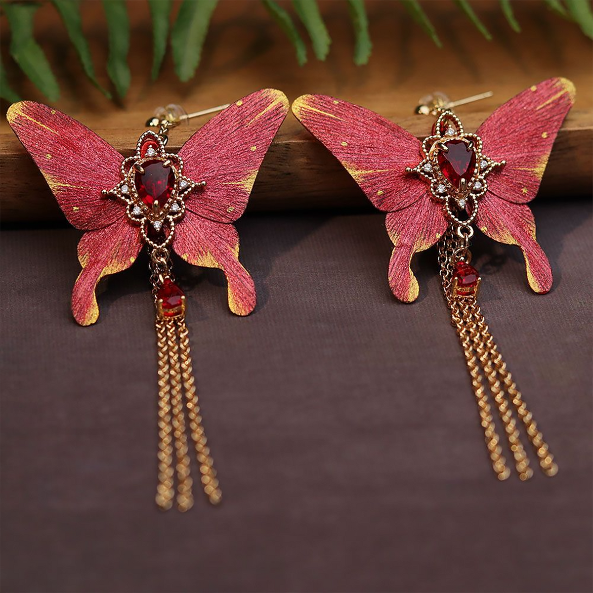 Close-up of a red silk butterfly earring with teardrop crystal and gold-toned setting