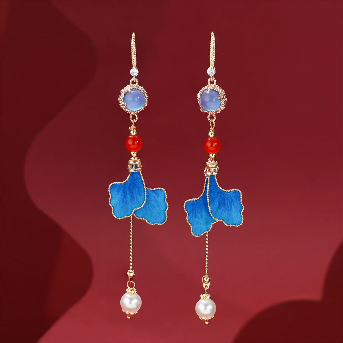 Blue leaf Ronghua drop earrings displayed on deep red fabric