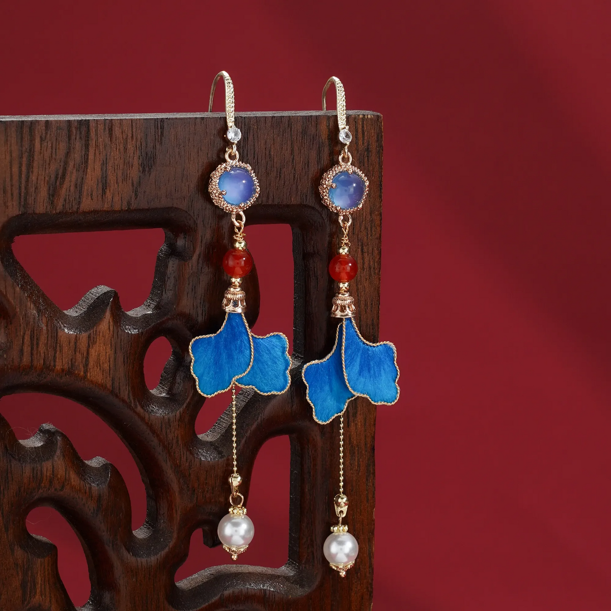 Blue Ronghua leaf earrings styled against carved dark wood and a red background
