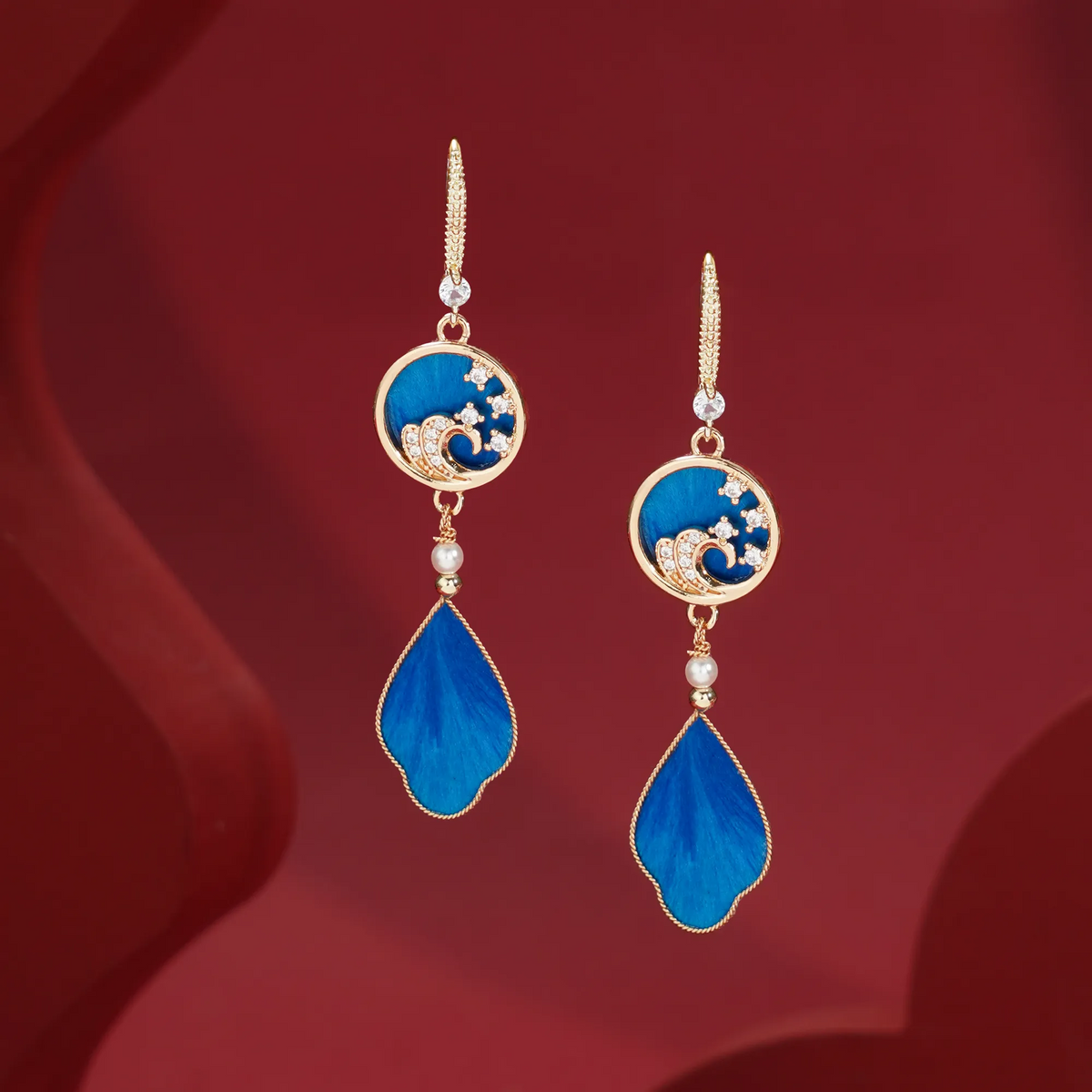 Handmade blue Ronghua wave earrings displayed on red fabric