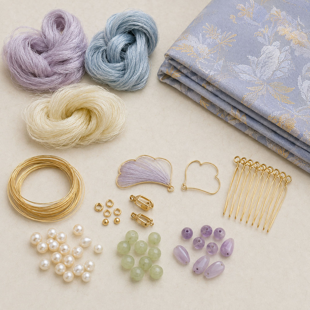 Coils of pale fibres, folded patterned fabric, beads, wire and metal findings arranged on a light surface.