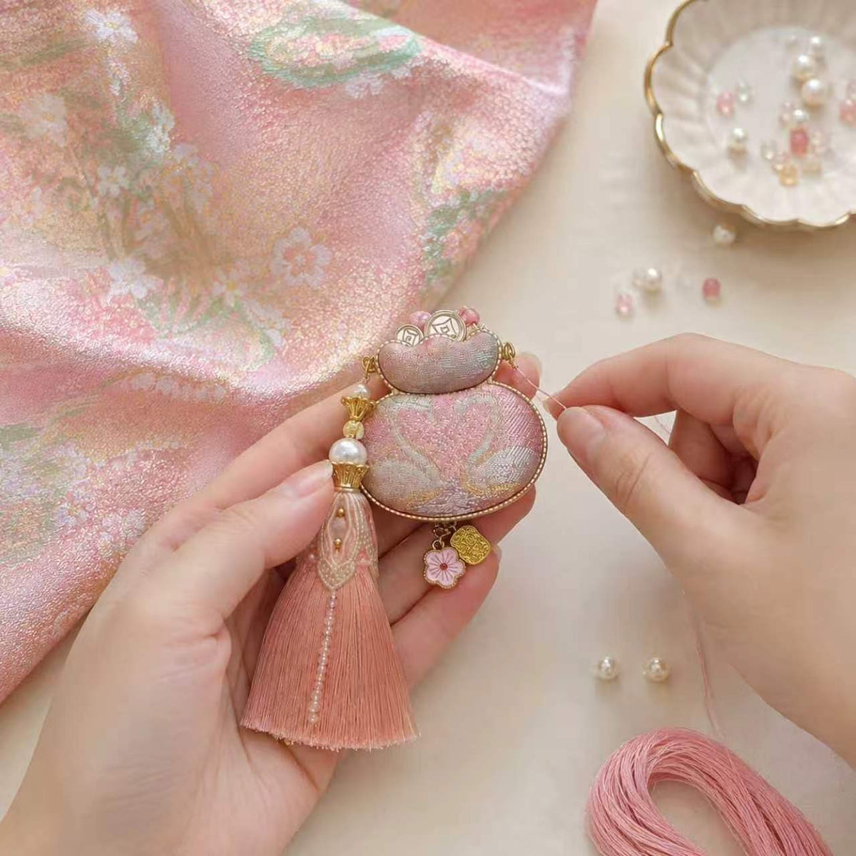 Hands holding a pink patterned textile ornament with a tassel.