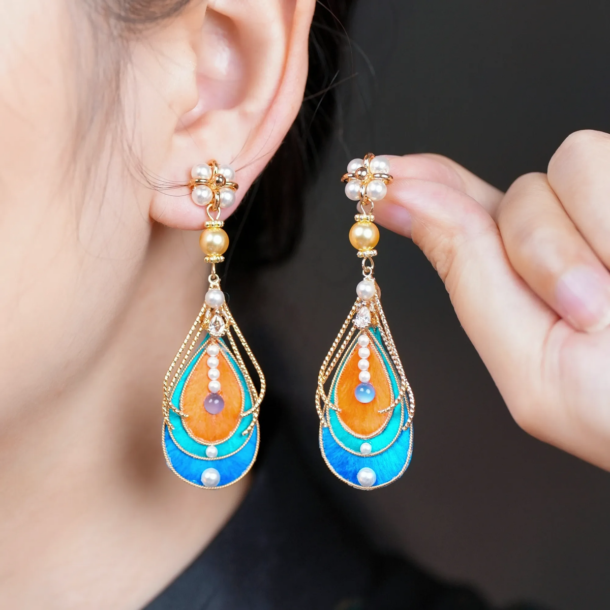 Model wearing handmade Dunhuang-inspired Ronghua drop earrings in orange, turquoise and blue