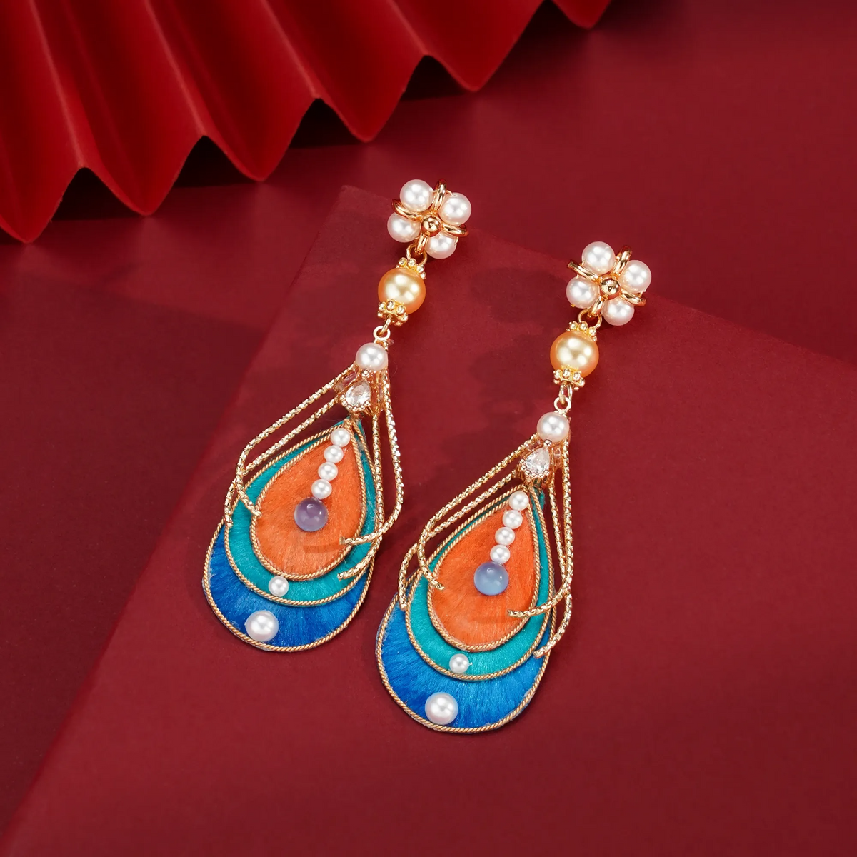 Handmade Ronghua drop earrings displayed on a deep red background