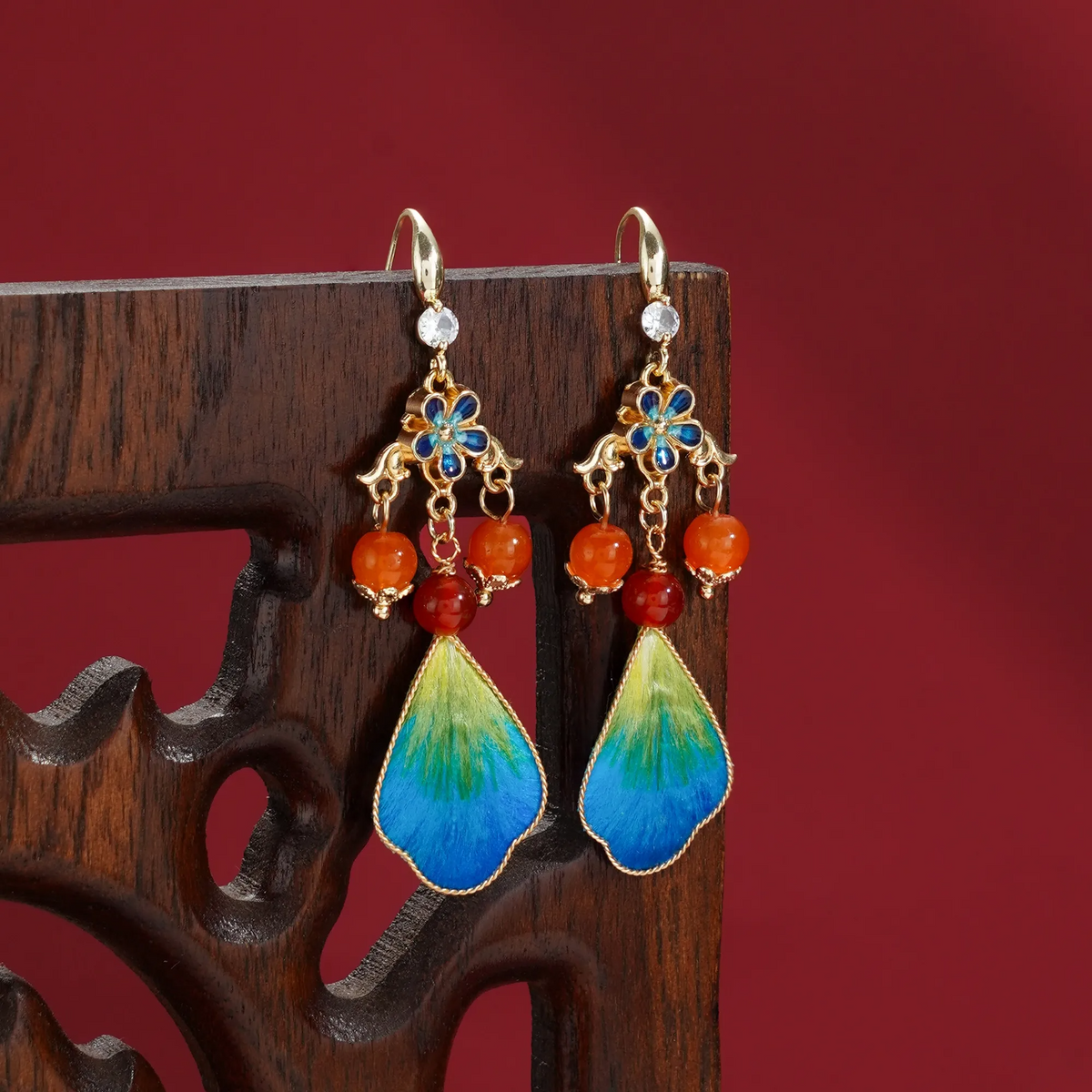 Ronghua silk-fibre drop earrings displayed on carved wood