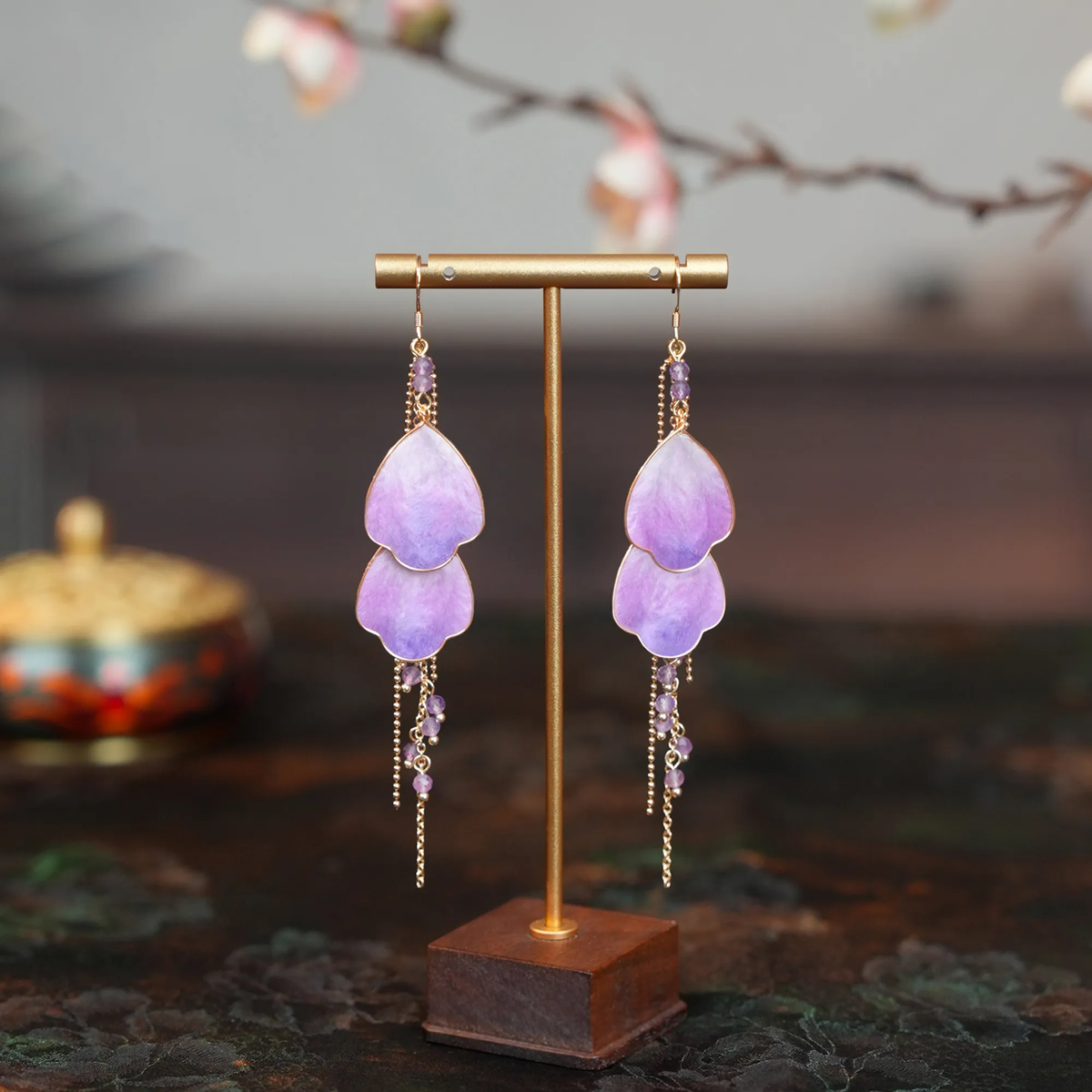 Model holding Wisteria Prelude Ronghua drop earring beside her ear, showing layered purple silk petals and gold tassel details